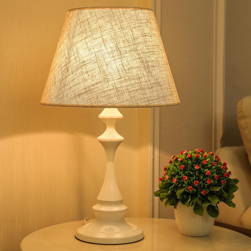 La lampe de chevet blanche et bois nordique allumée sur un meuble